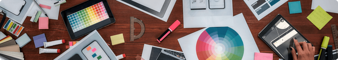 Desk with color wheel, color table, art supplies, and ipad showing logo design process